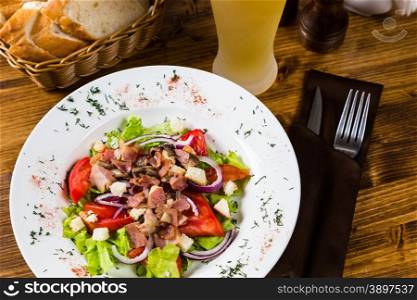 meat salad with spices and vegetables with light beer on on wooden table