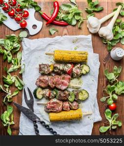 Meat Skewers for grill with vegetables and corn ears on rustic wooden background , top view