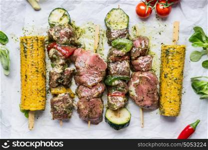 Meat Skewers for grill with vegetables and corn ears on white paper, top view, close up