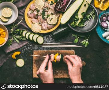 Meat skewers making. Female hands put meat on a skewer on wooden kitchen table background with chicken pieces and vegetables. Grill preparation