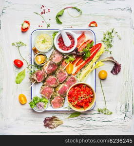 Meat skewers with fresh cutting vegetables and seasoning on enamel plate . Meat skewers for grill or cooking, preparation on light rustic background, top view
