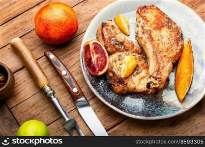 Meat steak, appetizing pork chop fried in a citrus marinade. Meat in the plate on wooden table. Pork steak roasted with citrus fruits.