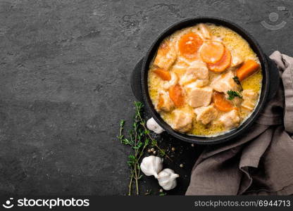 Meat stew, chicken fillet in sauce with carrot in a cast iron pot, top view