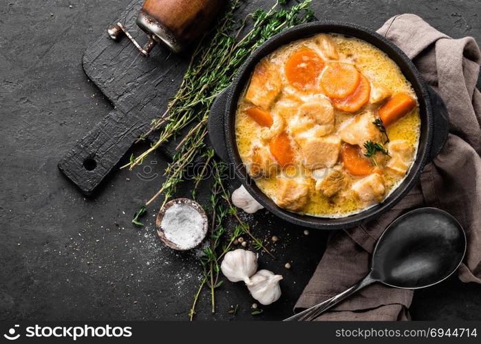 Meat stew, chicken fillet in sauce with carrot in a cast iron pot, top view