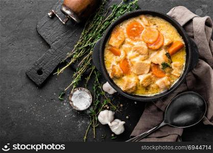 Meat stew, chicken fillet in sauce with carrot in a cast iron pot, top view