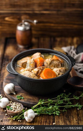 Meat stewed with carrots in sauce and spices in cast iron pot on dark wooden rustic background