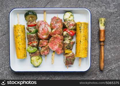 Meat, vegetables and corn Skewers in green herbs rubs and Marinades with Brush on gray concrete background, top view