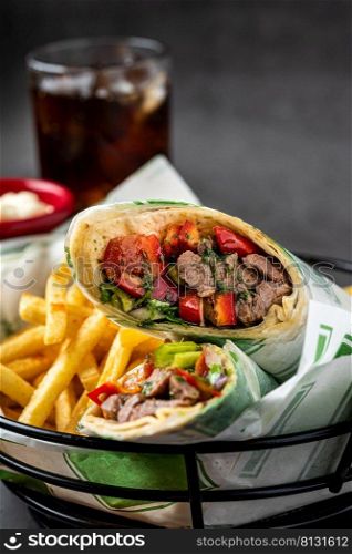 Meat wrap cut in half with french fries on dark stone table