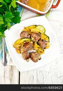 Meatballs baked with zucchini, cheese and nuts in a dish on a towel, parsley on a wooden board background from above