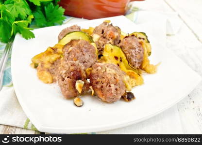 Meatballs baked with zucchini, cheese and nuts in a dish on a towel, parsley on a light wooden board background