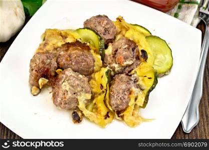 Meatballs baked with zucchini, cheese and nuts in a plate, napkin, garlic, parsley and fork on a dark wooden board background