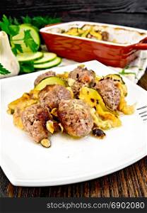Meatballs baked with zucchini, cheese and nuts in a plate, napkin, garlic, parsley and fork on a wooden plank background