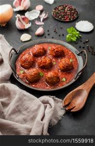 Meatballs in tomato sauce with pepper, garlic and parsley on black table background with wooden spoon