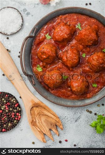 Meatballs in tomato sauce with pepper, garlic and parsley on light table with utensils. Top view