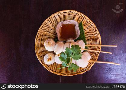 Meatballs toasted on wood basket dish and a cup of sauce decorated with coriander placed on the table dark wood. Top view