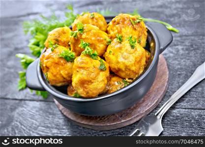Meatballs with tomato sauce in a black brazier, parsley, dill and fork on a wooden plank background