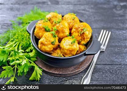 Meatballs with tomato sauce in a black brazier with parsley, dill, fork on a wooden plank background