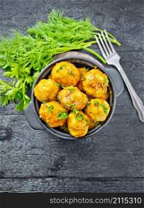 Meatballs with tomato sauce in a brazier with parsley, dill, fork on a wooden plank background on top