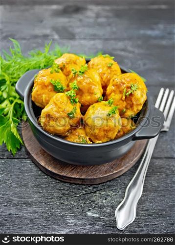 Meatballs with tomato sauce in a brazier with parsley, dill, fork on a wooden plank background