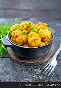 Meatballs with tomato sauce in a brazier with parsley, dill, fork on a black wooden board background