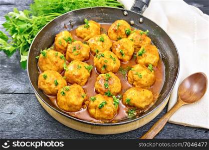 Meatballs with tomato sauce in a frying pan, parsley, dill, towel and spoon on a black wooden board background