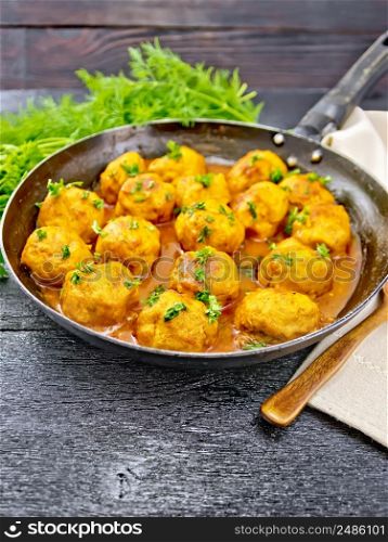 Meatballs with tomato sauce in a frying pan with parsley greens, dill, towel and spoon on a black wooden board background