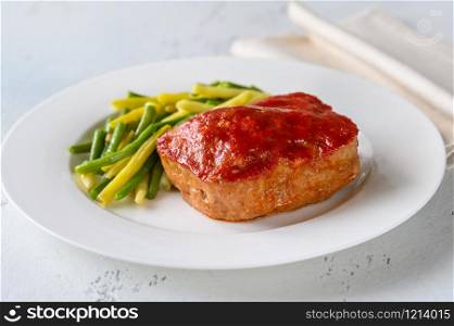 Meatloaf topped with tomato sauce with green beans