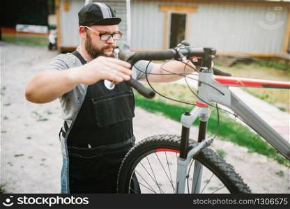 Mechanic adjusts the bicycle handlebars and brakes. Cycle workshop outdoor. Bicycling sport, bearded service man work with wheel. Mechanic adjusts the bicycle handlebars and brakes
