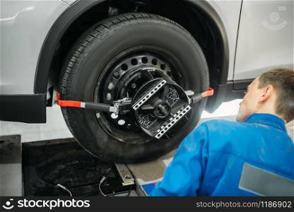 Mechanic adjusts the target on collapse of convergence stand in auto-service. Computer diagnostic of car suspension. Mechanic adjusts collapse of convergence stand