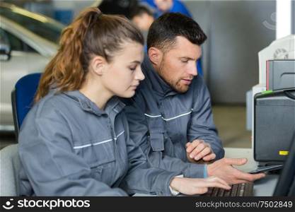 mechanic and apprentice sat at computer desk looking at smartphone