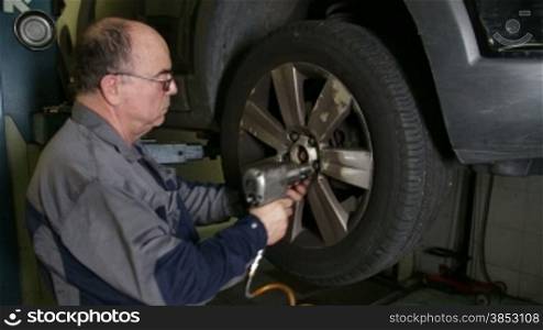 Mechanic changes a car wheel.Repairman removing screws from a wheel rim with a pneumatic gun.Mechanic doing a car review.