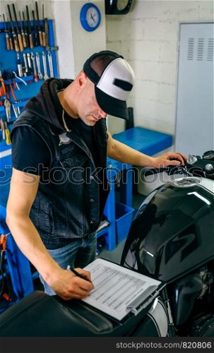 Mechanic checking motorcycle and taking notes. Mechanic checking motorcycle