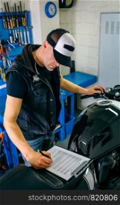 Mechanic checking motorcycle and taking notes. Mechanic checking motorcycle