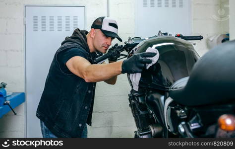 Mechanic cleaning a customized motorcycle in his workshop. Mechanic cleaning a motorcycle