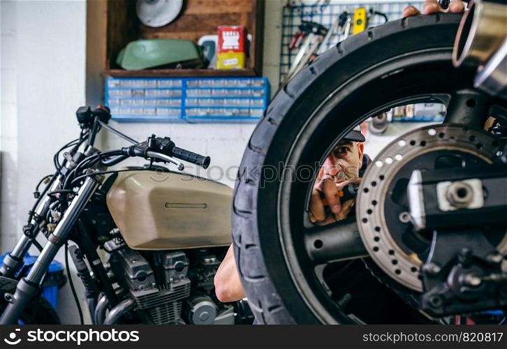 Mechanic fixing custom motorcycle wheel in his workshop. Selective focus on mechanic in background. Mechanic fixing custom motorcycle wheel