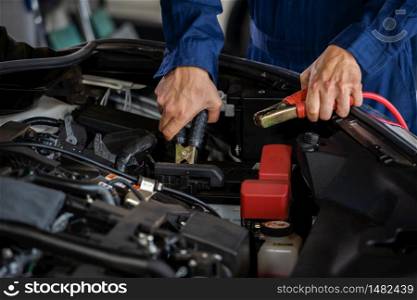 mechanic hand charging battery of a car with electricity through jumper cables