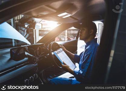 Mechanic holding clipboard and checking inside car to maintenance vehicle by customer claim order in auto repair shop garage. Repair service. People occupation and business job. Automobile technician