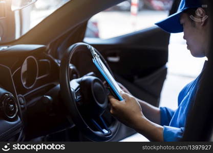 Mechanic holding clipboard and checking inside car to maintenance vehicle by customer claim order in auto repair shop garage. Repair service. People occupation and business job. Automobile technician