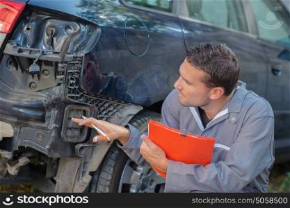 Mechanic holding clipboard assessing car