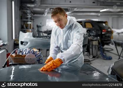 Mechanic in uniform sanding painted car body. Painter assesses hood surface damage. Mechanic in uniform sanding painted car body