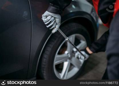 Mechanic in uniform unscrews the wheel in tire service. Man repairs car tyre in garage, automobile inspection in workshop. Mechanic unscrews the wheel in tire service