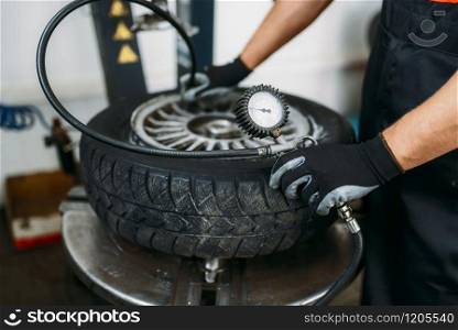 Mechanic inflates the wheel, tire repairing service. Man repairs car tyre in garage, professional automobile inspection in workshop