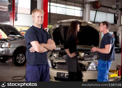 Mechanic looking at camera with customer and second mechanic in background