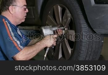 Mechanic mounting a car wheel.Repairman inserting screws into a wheel rim with a pneumatic gun.Mechanic doing a car review.