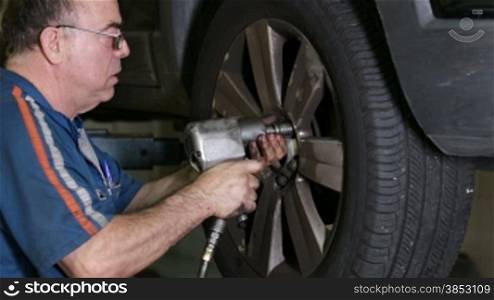 Mechanic mounting a car wheel.Repairman inserting screws into a wheel rim with a pneumatic gun.Mechanic doing a car review.