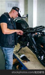 Mechanic repairing customized motorcycle by changing a fuse in the workshop. Motorcycle mechanic changing a fuse