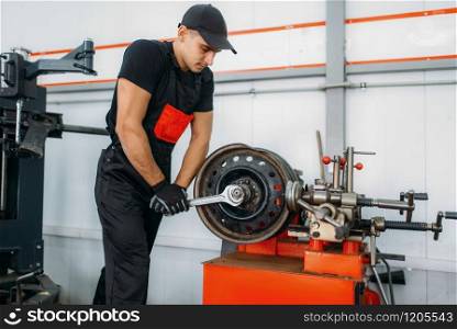 Mechanic repairs a crumpled disc, tire repairing service. Man fixing car tyre in garage, professional automobile inspection in workshop. Mechanic repairs a crumpled disc, tire service