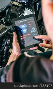 Mechanic reviewing motorcycle with a tablet app in the workshop. Motorcycle mechanic using tablet app