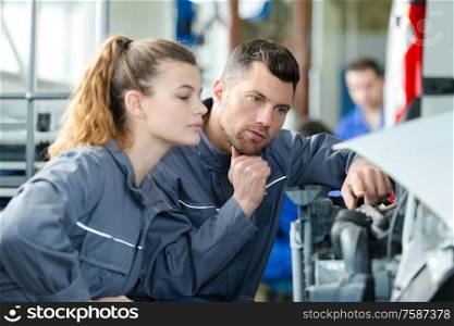 mechanic showing female trainee under the hood of the car
