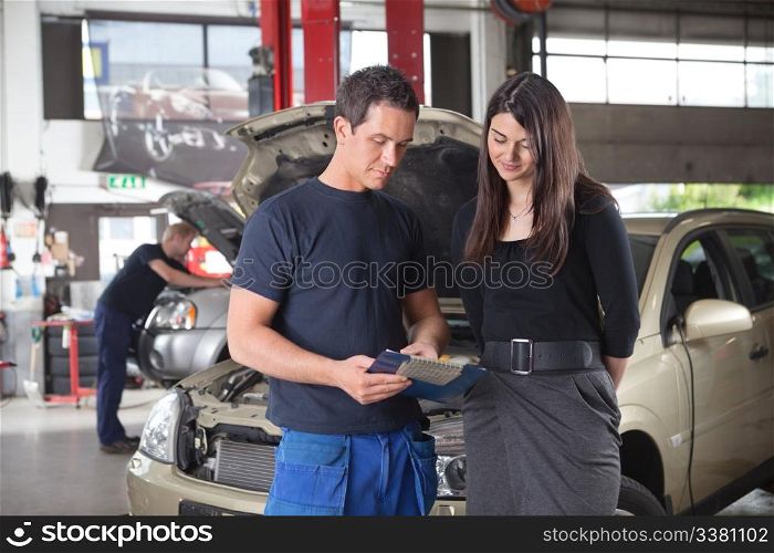 Mechanic showing the cost of service to female client while man working in background